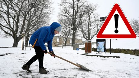 Muž odhŕňa sneh zo zasneženej cesty.