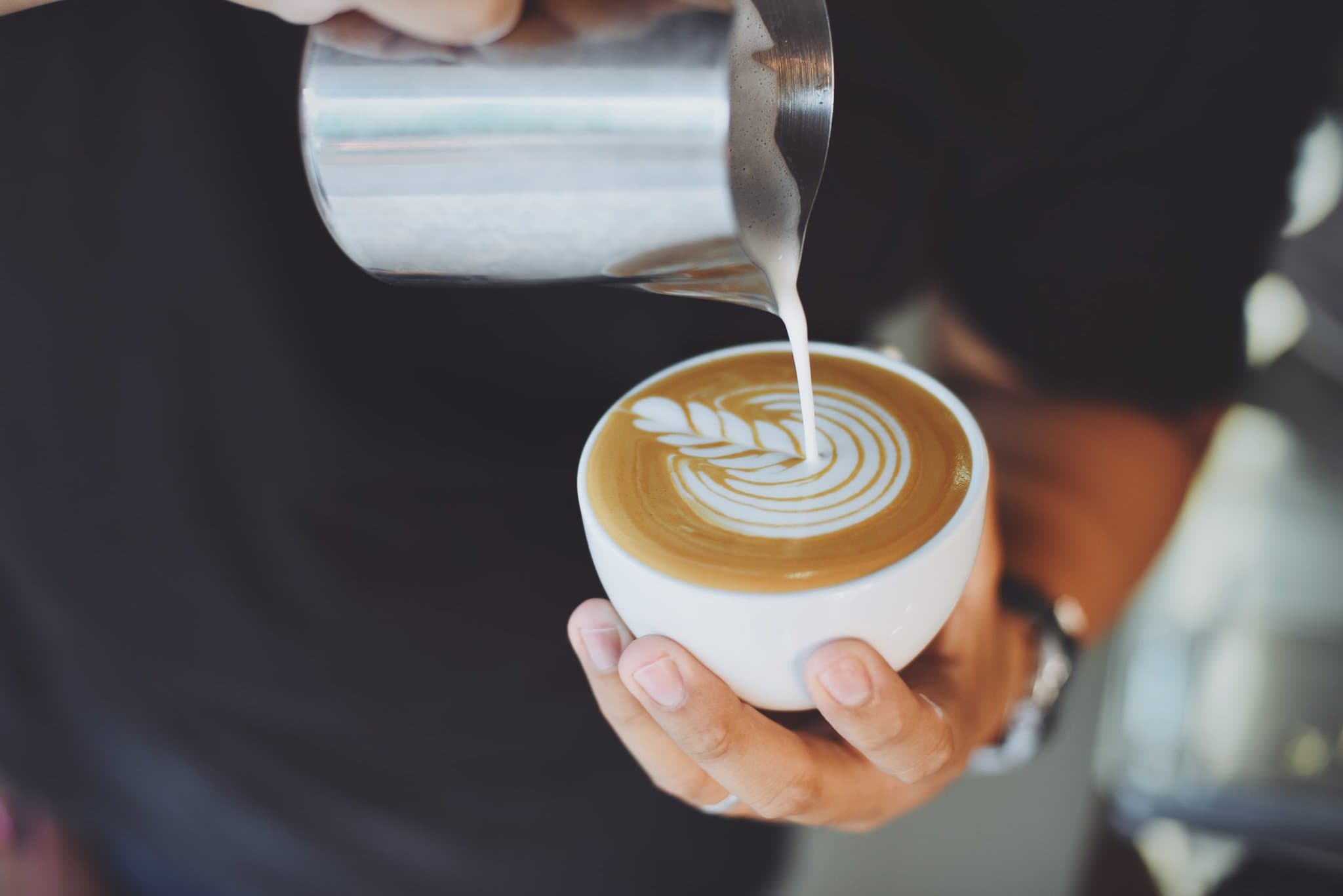 person-serving-cup-coffee-with-metal-jug